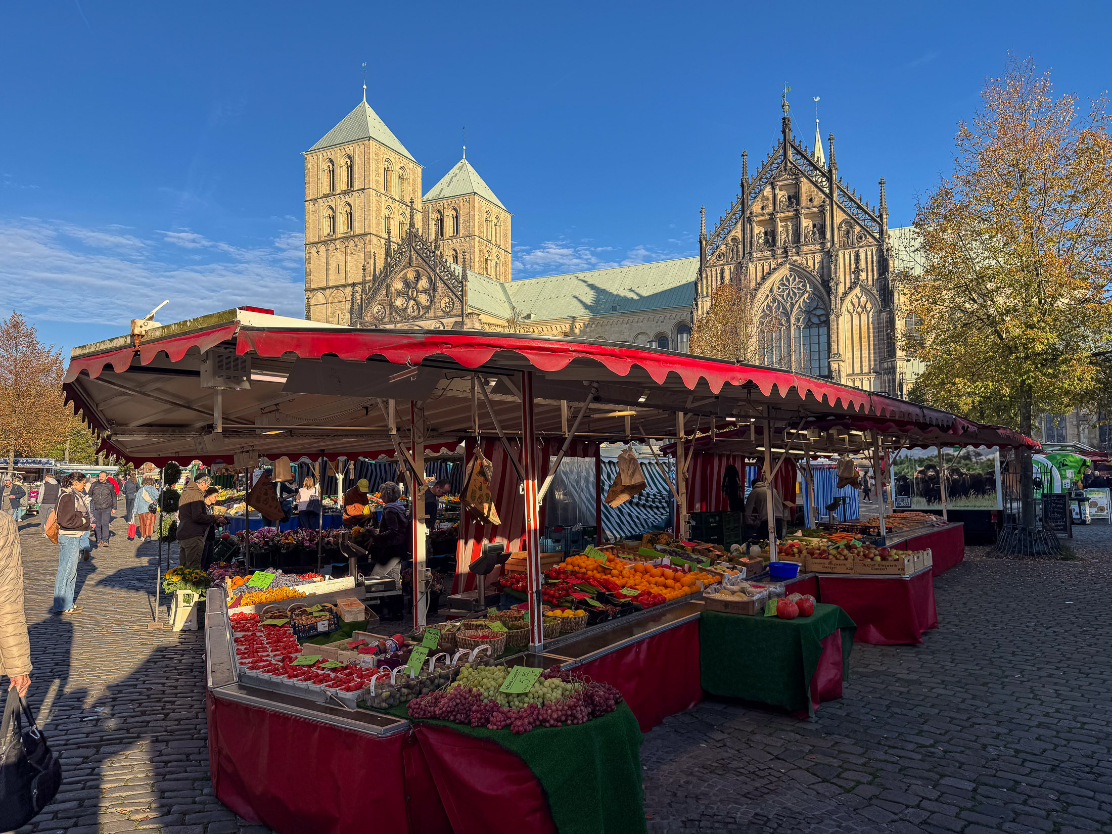 Queransicht eines Obst- und Gemüsestands mit Domtürmen im Hintergrund