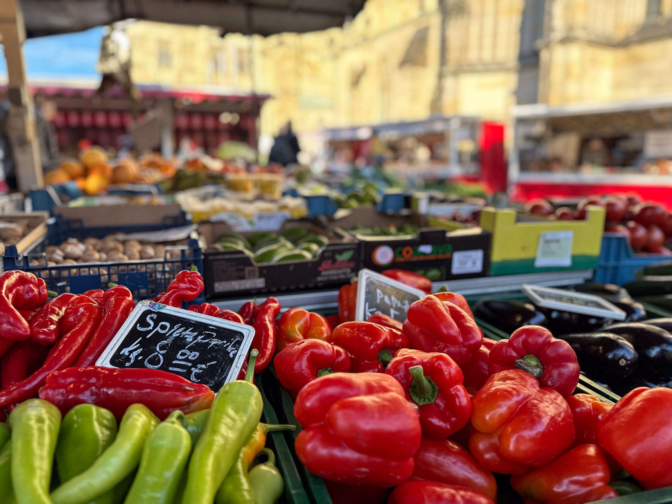 Rote und grüne Paprika in Kisten, mit weichem Dom- und Marktstandhintergrund