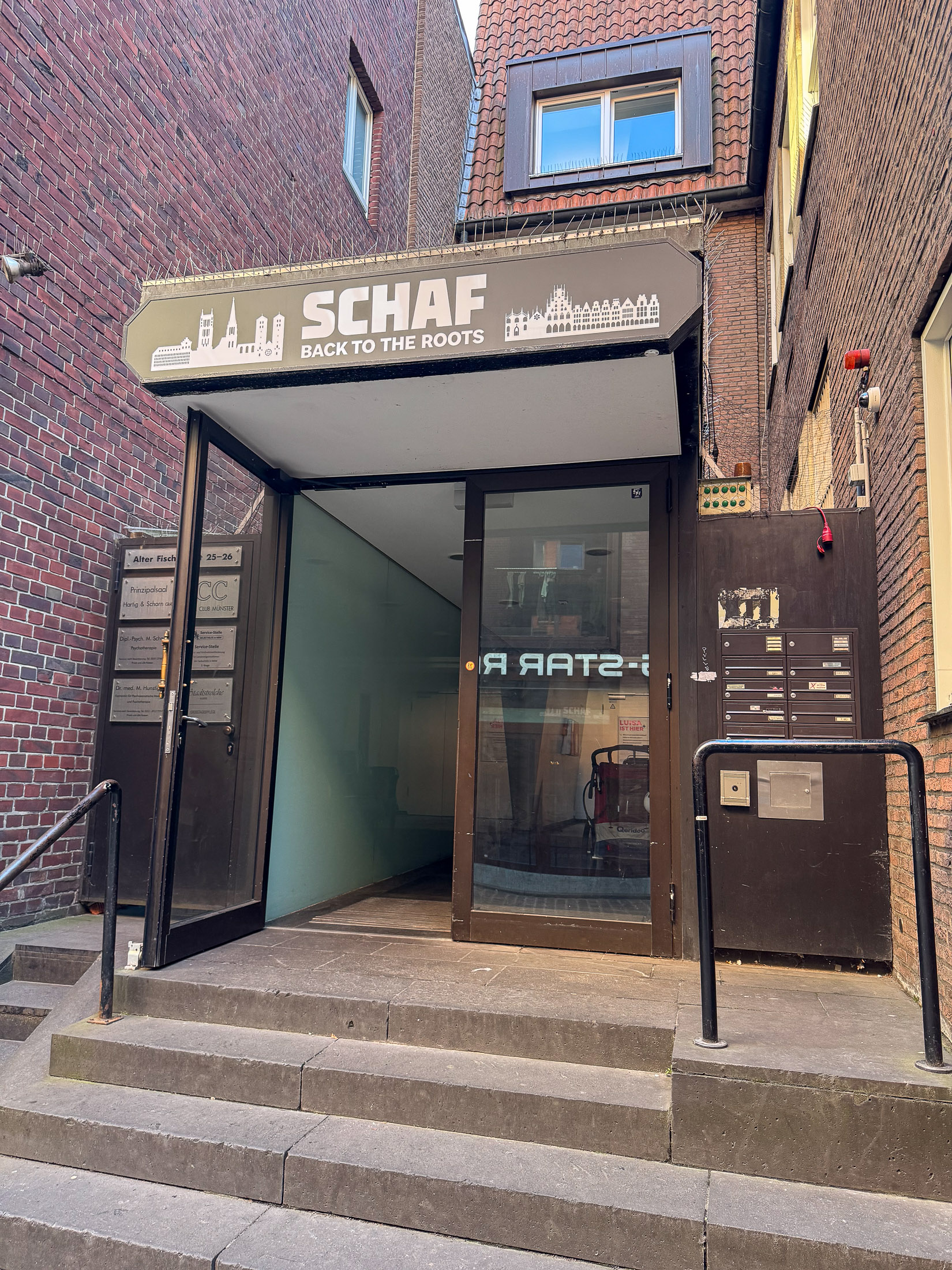 Stufen zum Eingang des SCHAF mit dem Schriftzug Back to the Roots an der Backsteinfassade