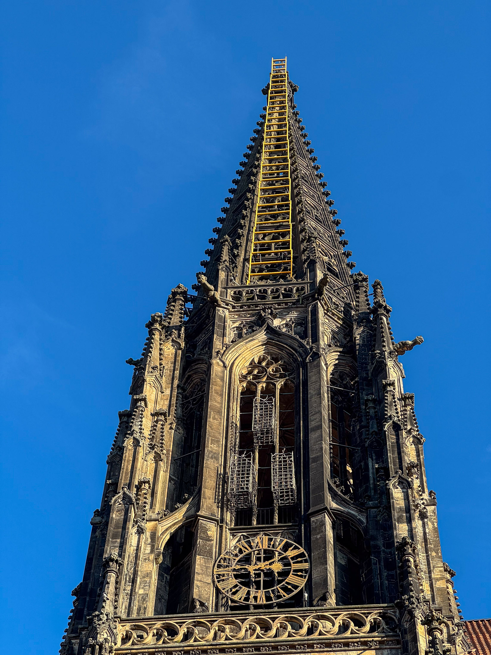 Turm von St. Lamberti mit Uhr und gelber Leiter vor blauem Himmel