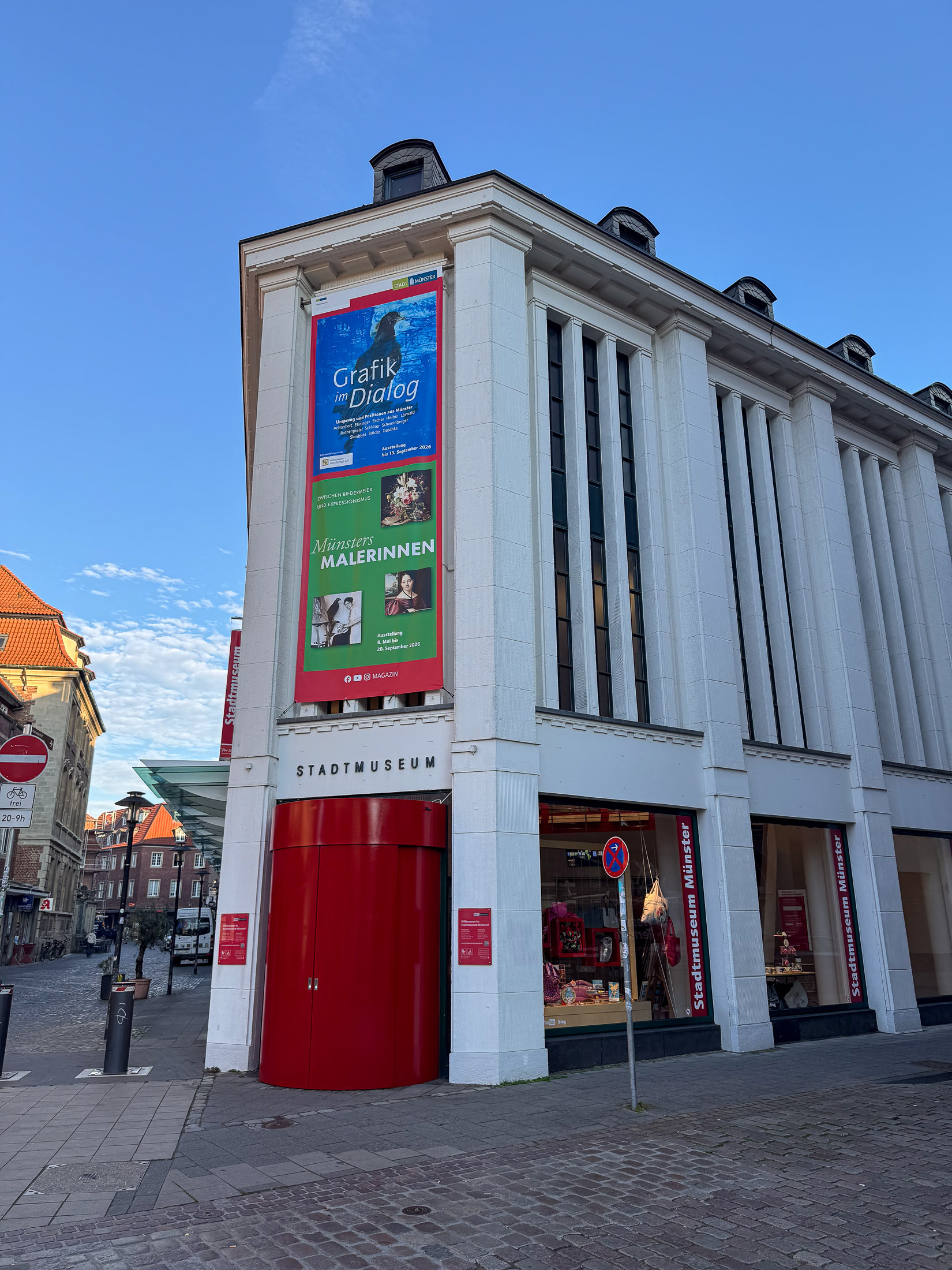 Weißes Gebäude des Stadtmuseums Münster mit rotem Eingang und Ausstellungsbannern
